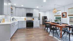 A modern kitchen with white cabinets, stainless steel appliances, and a dining area with a wooden table and black chairs. - Ms Dot’s 290 Wine Trail Farmhouse-Downtown- Fire Pit - Covered Patio (Johnson City)