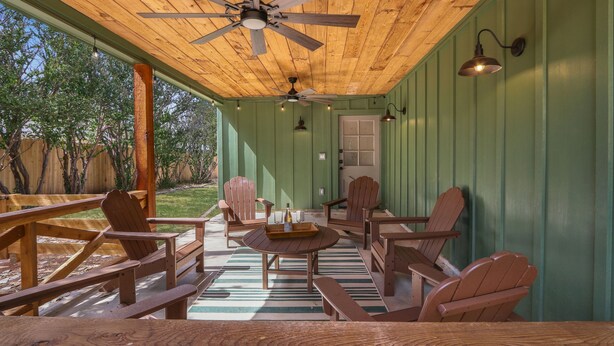 A covered patio with wooden furniture, a ceiling fan, and wall-mounted lights. - Ms Dot’s 290 Wine Trail Farmhouse-Downtown- Fire Pit - Covered Patio (Johnson City)