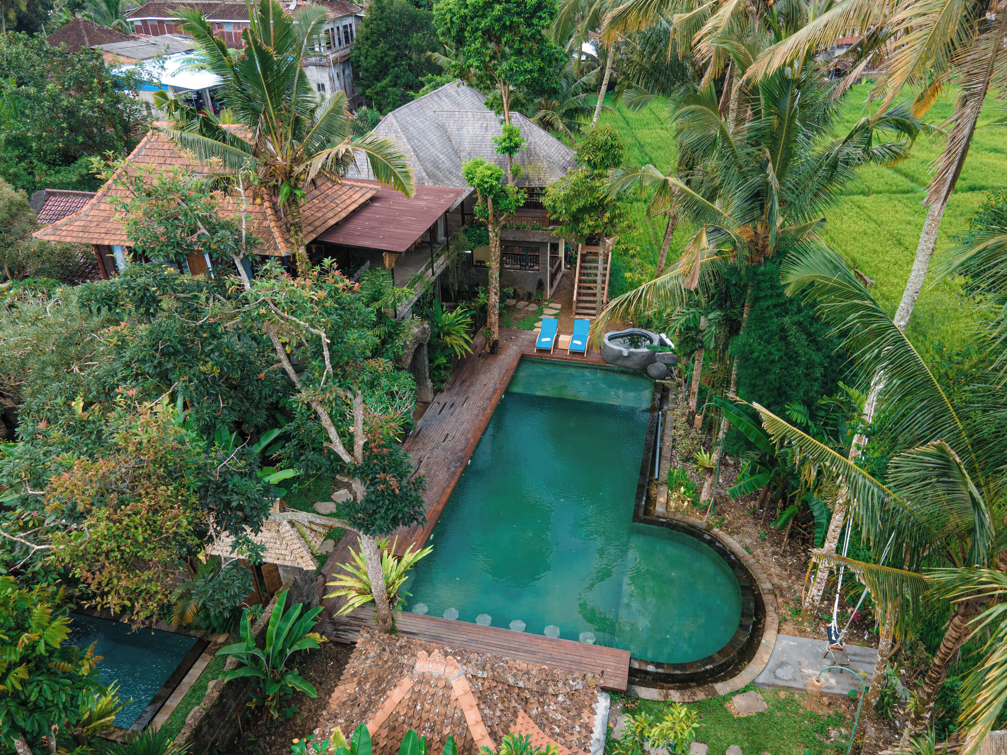 An aerial view of a residential property with a swimming pool, a wooden deck, and lush greenery.
