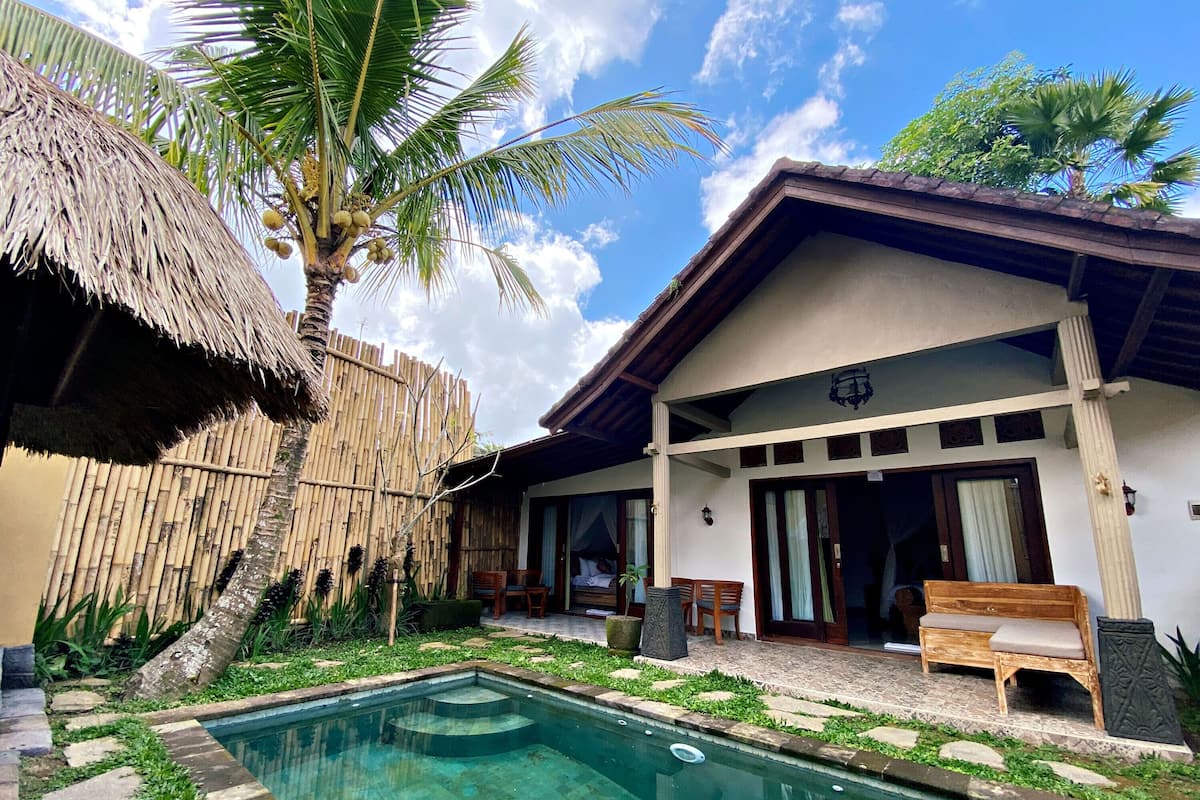 A poolside area with a thatched roof, a wooden deck, and a house with a balcony.