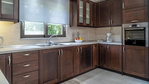 A modern kitchen with dark wood cabinets, stainless steel appliances, and a large window. - Villa Emily (Voukolies, Chania)