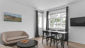 A modern living room with a sofa, a dining table with chairs, a flat-screen TV, and a painting on the wall.