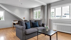 Ett modernt vardagsrum med en grå soffa, ett soffbord, ett matbord med stolar och stora fönster med gardiner.