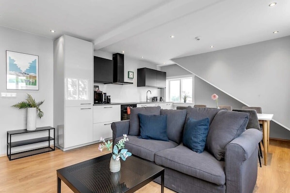 A modern living room with a grey sofa, a black coffee table, and a kitchen in the background.