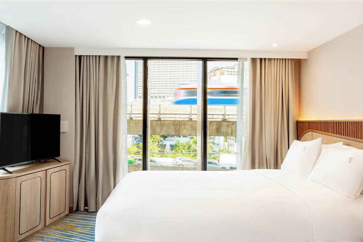 Een hotelkamer met een bed, een televisie op een houten kast, en uitzicht op een passerende trein.