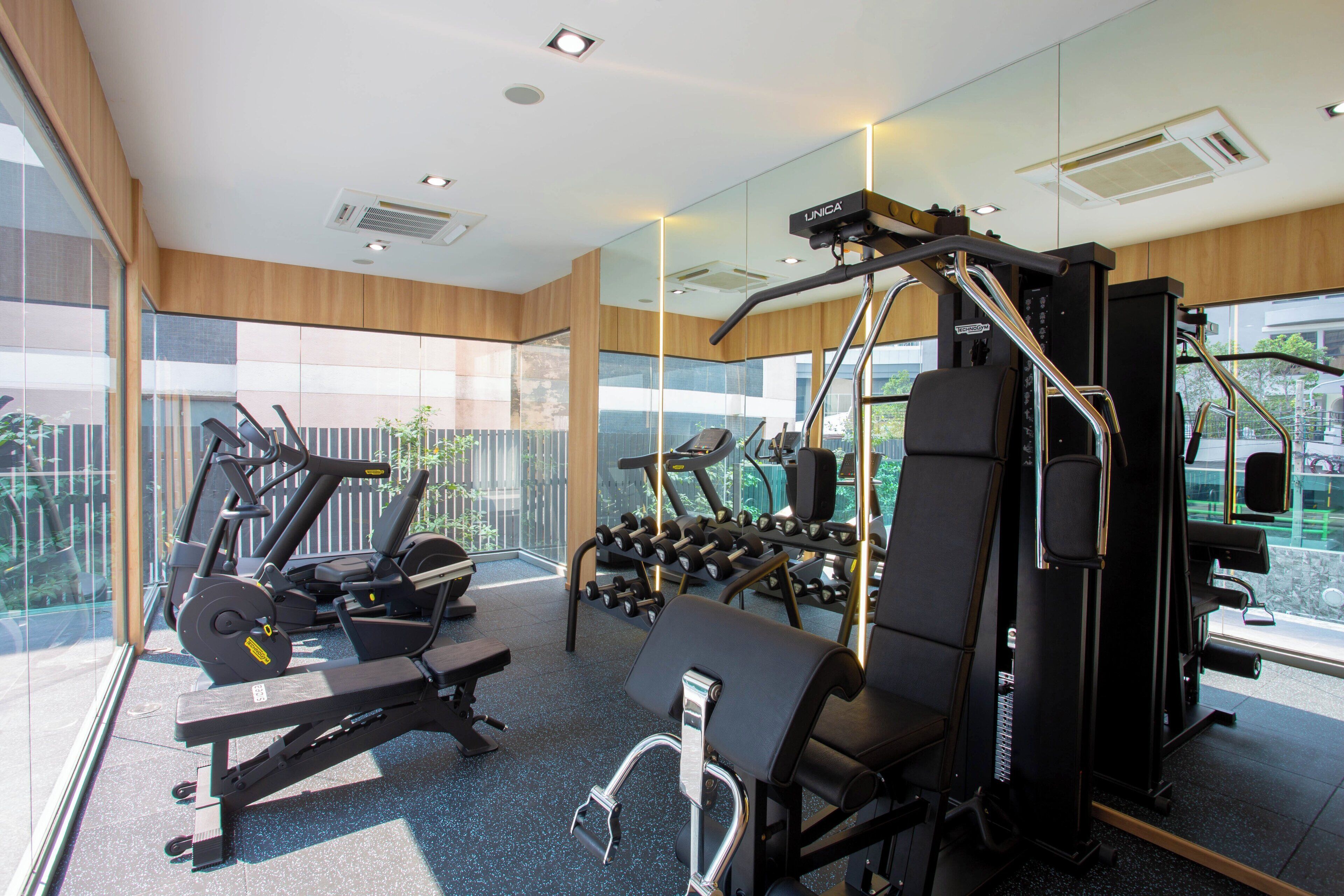 A modern gym with various exercise equipment, large windows, and a view of the outdoors.