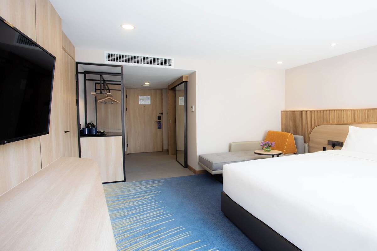 Une chambre d’hôtel dotée d’un grand lit, d’une télévision, d’un bureau et d’un coin salon avec un canapé et un fauteuil.