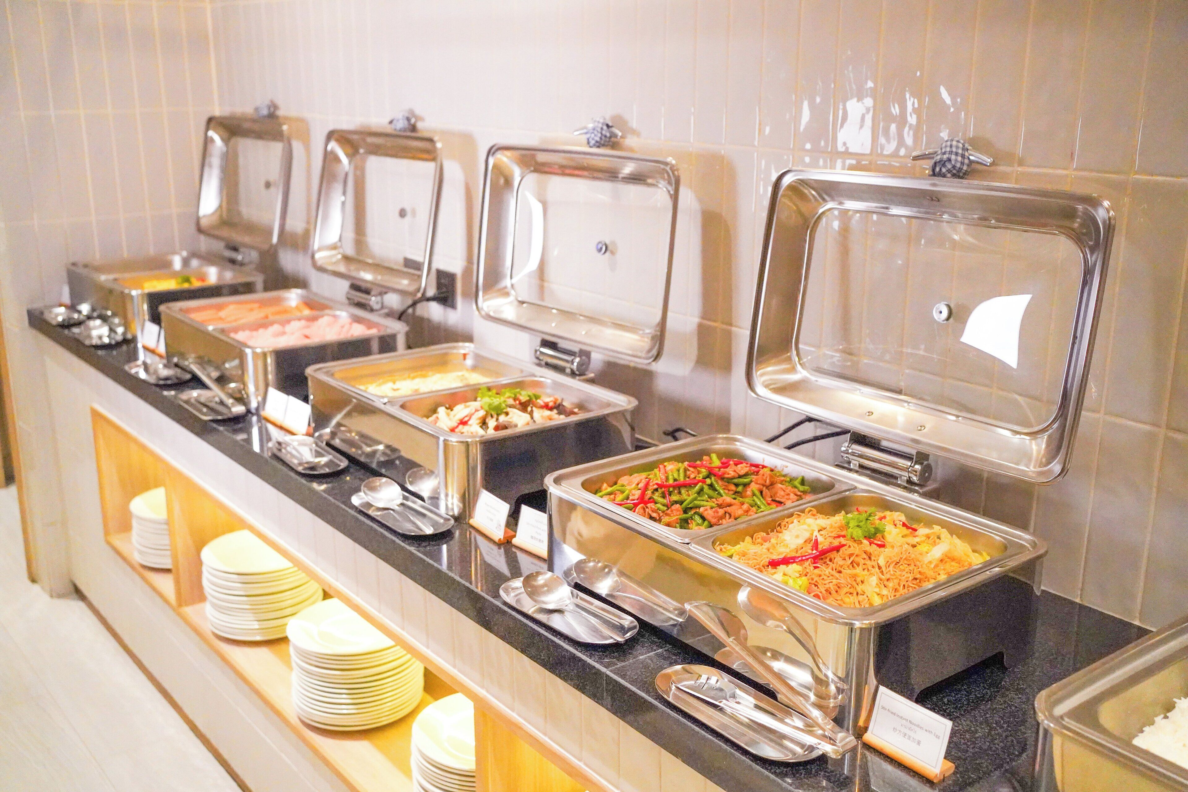 Un buffet proposant une variété de plats, présentés sur différents présentoirs recouverts d’une cloche en verre transparente et portant une étiquette indiquant leur nom.