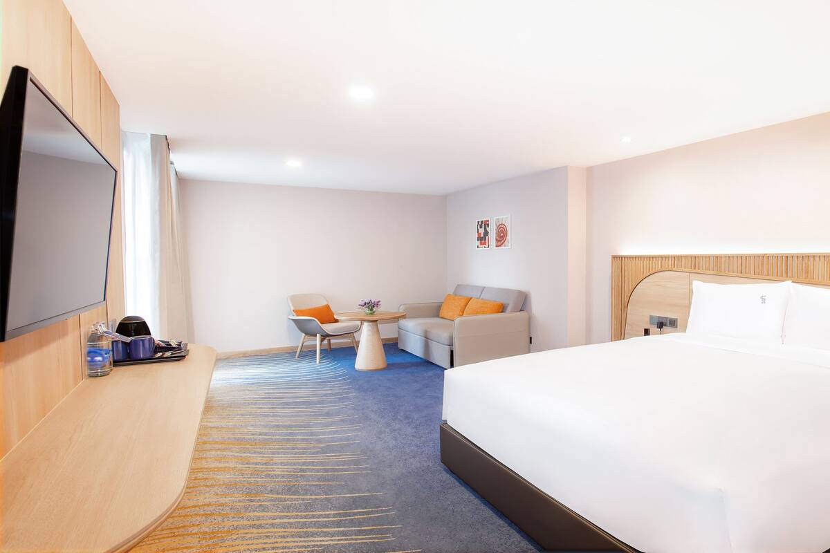 Een hotelkamer met een bed, een bureau met stoel, een televisie en een klein tafeltje met een vaas.