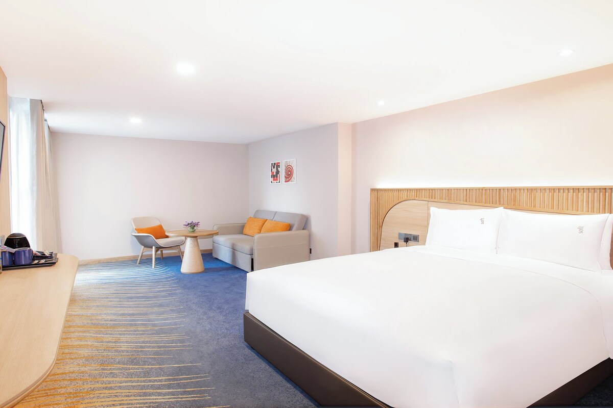 Une chambre d’hôtel comprenant un lit, un bureau avec une chaise, une télévision et une petite table avec un vase.