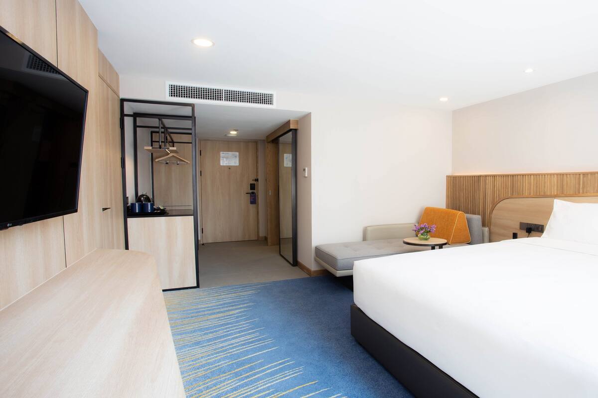 Hotelkamer met een groot bed, een televisie, een bureau en een zithoek met een bank en fauteuil.