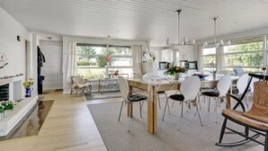 Ein geräumiger Essbereich mit einem großen Tisch und Stühlen, im Hintergrund eine Küche und große Fenster, die für natürliches Licht sorgen.