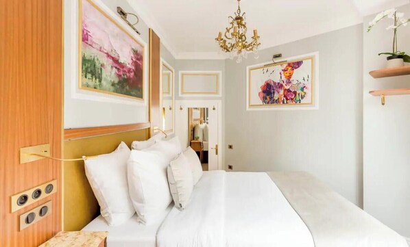 Une chambre d’hôtel avec un grand lit, un lustre et des œuvres d’art aux murs.
