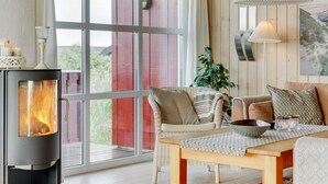 A cozy room with a fireplace, large windows, a wooden table, and comfortable seating.