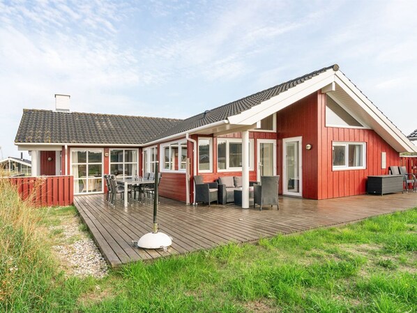 Ein rotes Holzhaus mit einer großen Terrasse, einem Essbereich und einer Veranda mit Gartenmöbeln.