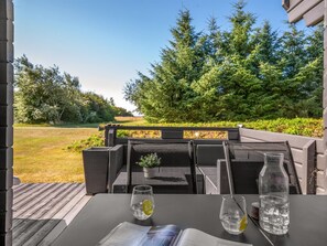 Un espace extérieur aménagé avec des sièges et offrant une vue sur une forêt, une table avec deux verres d’eau et un menu.