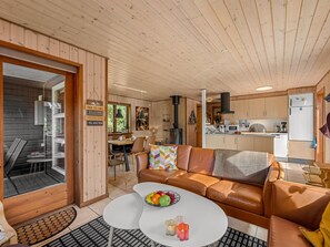 Interior acollidor d'una cabana amb zona de menjador, un sofà, una taula de cafè amb fruita i una cuina al fons.