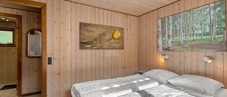 A wooden-paneled room with a bed, a painting of a flower, and a forest view.