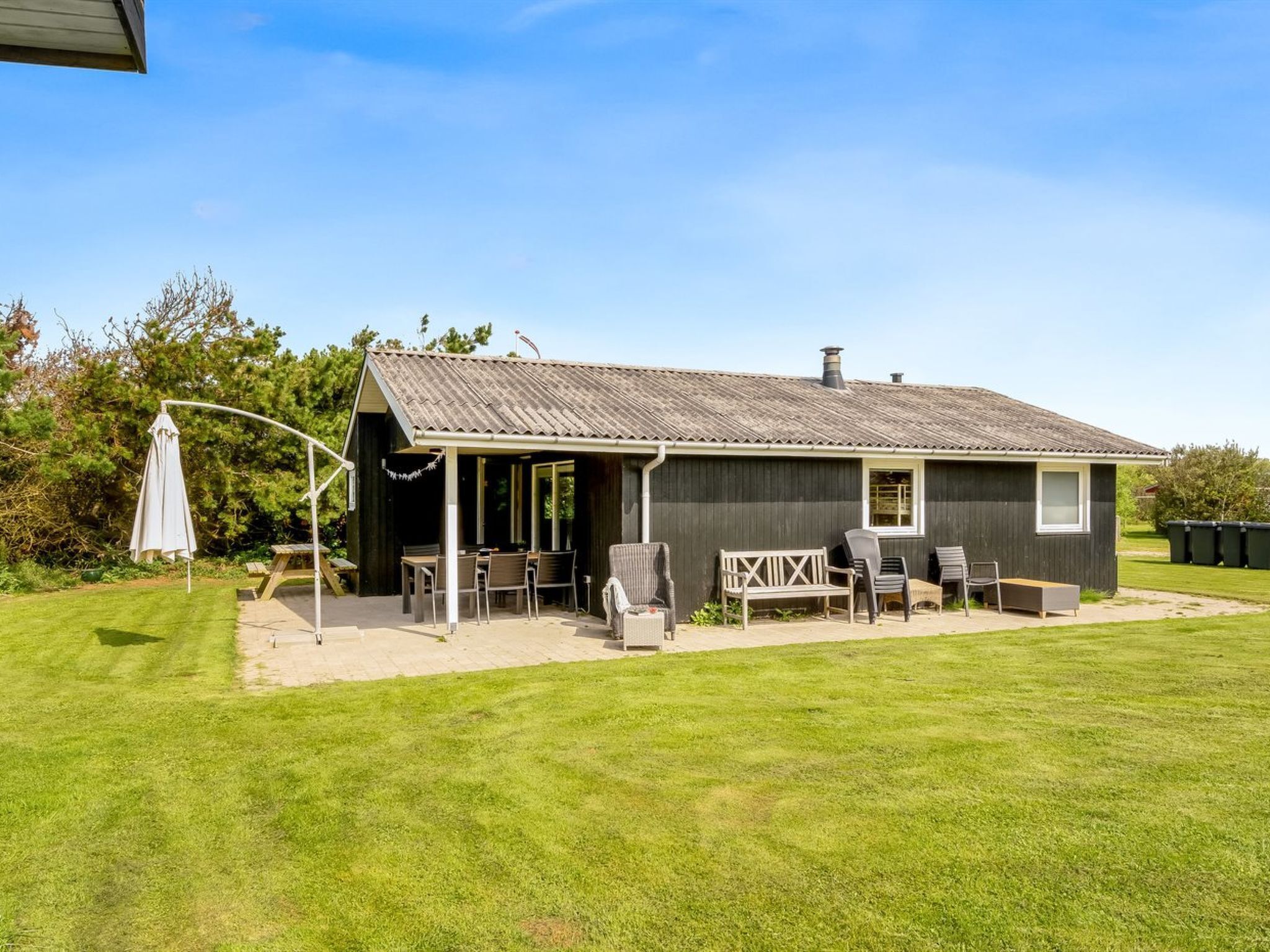 A small, single-story building with a covered patio area, outdoor seating, and a lawn.
