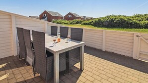 En terrasse med et bord, stole, en vinflaske og et vinglas.