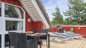 En träaltan med ett bord och stolar, en grill och solstolar.