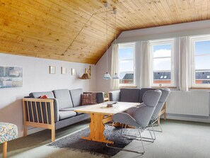 A modern loft bedroom with a sloped ceiling, a wooden dining table, grey upholstered seating, and large windows. - "Lynne" - 2.3km from the sea by Interhome (Rømø)
