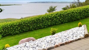 A landscaped garden with a pebble path, green hedges, and a view of a large body of water.
