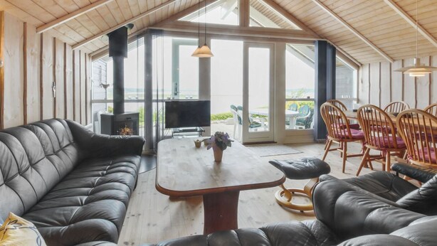 A cozy room with a wooden ceiling, a fireplace, a TV, and a dining area with chairs.