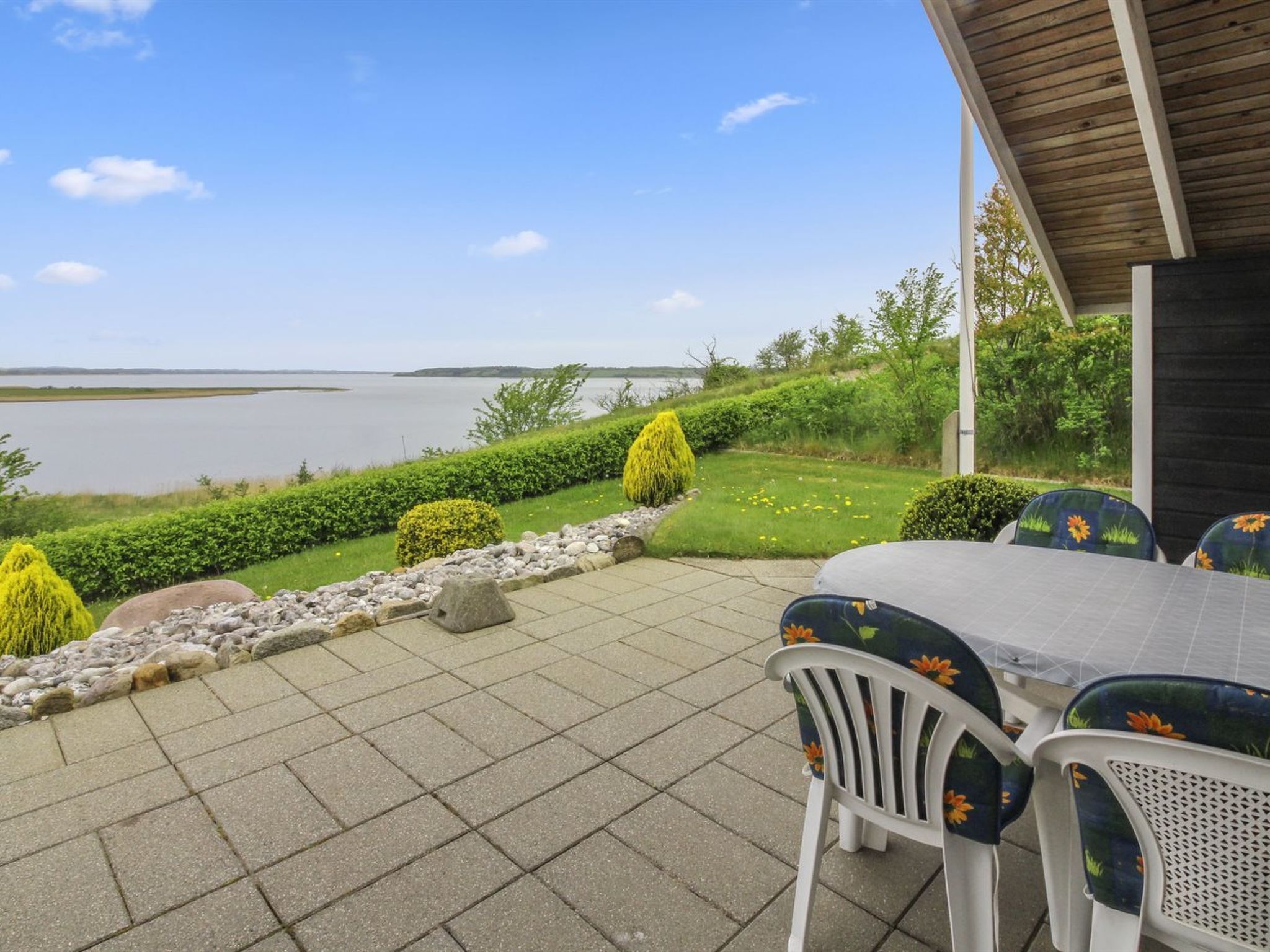 Un patio al aire libre con vista a un lago, una mesa con sillas y una pérgola de madera.