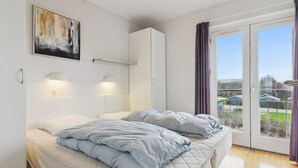 A bedroom with a bed, a painting on the wall, and a view through the window.