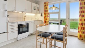 A modern kitchen with white cabinets, a built-in oven, and a dining area with a round table and chairs.
