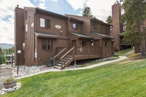 A brown multi-story building with a staircase leading to the entrance, a bike parked outside, and a clear sky. - Snowflake Condo | Ski-Out to Chairlift (Breckenridge)