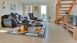 Un salon moderne avec un canapé, deux fauteuils en cuir noir, une table basse et un escalier en bois.
