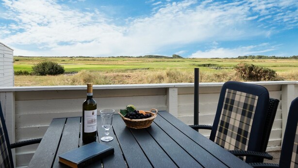 Une table avec une bouteille de vin, un verre et un panier de raisins, sur un balcon donnant sur un terrain de golf.
