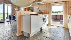 A modern kitchen with a central island, wooden ceiling, and large windows offering a view of the outdoors.
