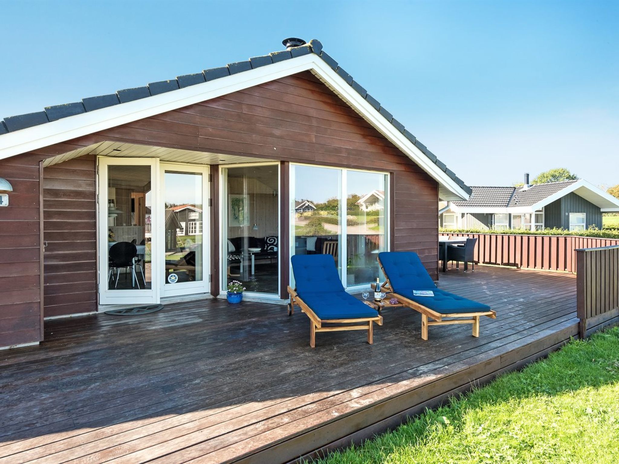 Une terrasse en bois avec deux chaises longues bleues et une porte vitrée donnant sur un espace intérieur.