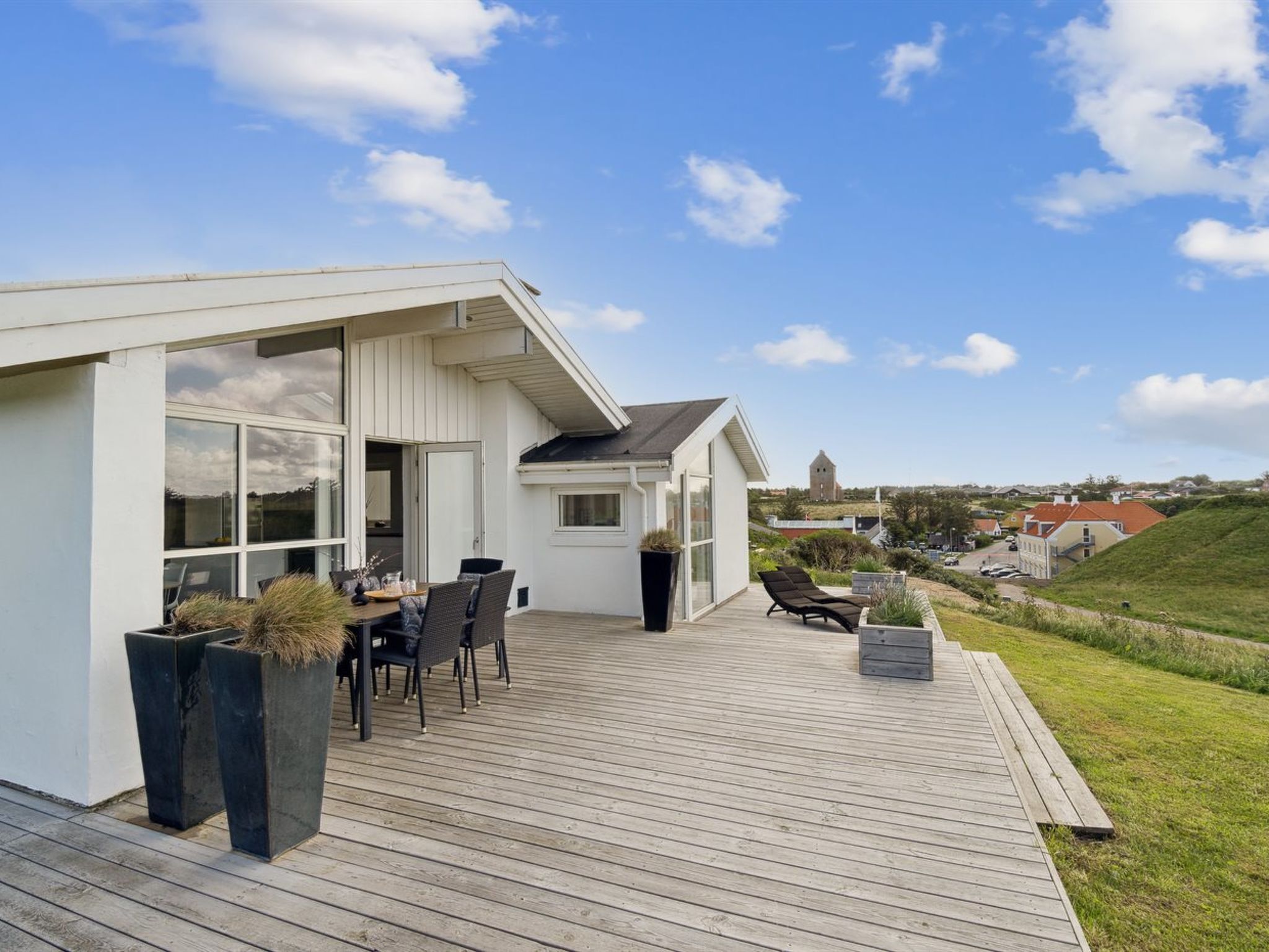 Ett modernt hus med en träaltan, utomhusmöbler och utsikt över det omgivande landskapet.