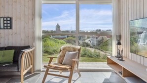 A modern living room with a large sliding glass door leading to a balcony, a wooden chair with a fur throw, a black leather sofa, and a flat-screen TV on a wooden shelf. - "Ohto" - 281m from the sea by Interhome (Hjørring)