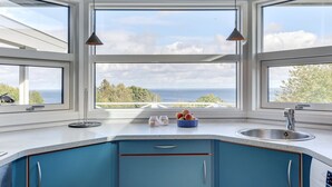 A kitchen with blue cabinets, a white countertop, and a large window overlooking the sea. - "Tjelle" - 300m from the sea by Interhome (Allinge)