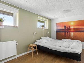 Un dormitorio con cama, un taburete pequeño, un radiador y un estante con una planta.
