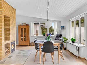 Una cocina moderna con chimenea de ladrillo, una mesa de comedor con sillas y vistas al exterior a través de amplias ventanas.