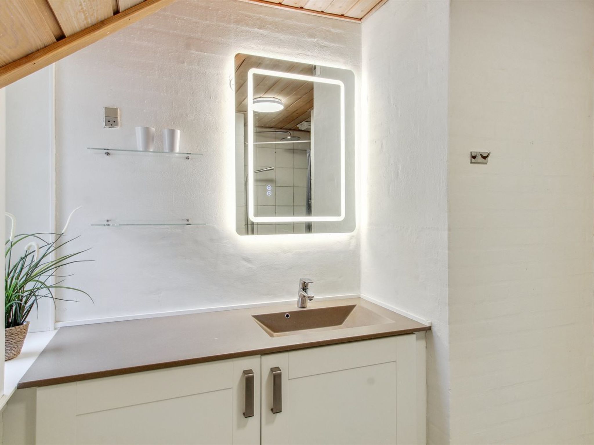Une salle de bain dotée d’un lavabo moderne, d’un miroir avec éclairage intégré et d’une plante en pot.