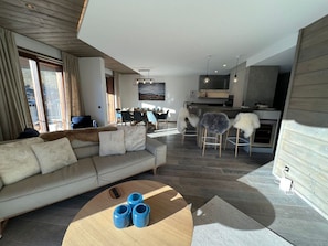 A modern living room with a sofa, a coffee table, and a dining area with chairs and a kitchen in the background.