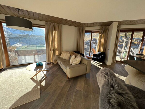 A spacious living room with a sofa, a black chair, and a fur rug. Large windows offer a view of a snowy landscape. - Stylish Penthouse in Tignes Lavachet, 4 Bedrooms, WiFi, 8 People (Tignes)