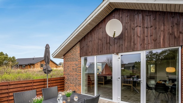 Eine Holzterrasse mit Tisch und Stühlen, einer Satellitenschüssel und einer Glastür zu einem Innenbereich.