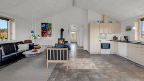 Eine moderne Küche mit Herd, Backofen und Schränken, ein Wohnbereich mit Sofa und Couchtisch, sowie ein großes Fenster.