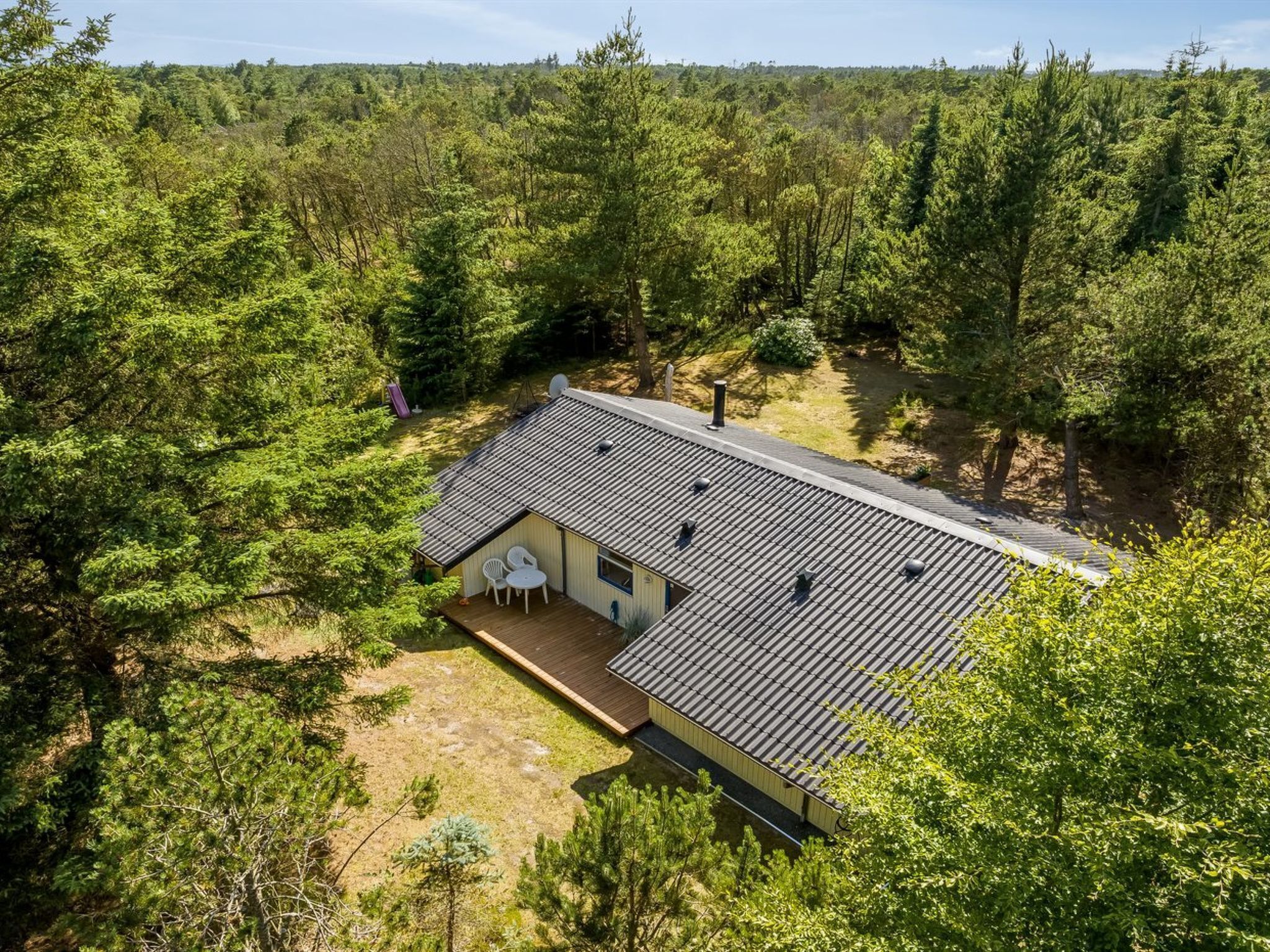 A single-story house with a sloped roof, surrounded by dense forest.