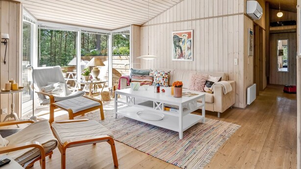 A spacious living area with a large window, a white sofa, a coffee table, and a wooden ceiling.
