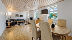 Ett modernt vardagsrum med ett träpanelat tak, en soffa, ett matbord med stolar och en tv.
