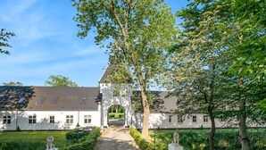 En vit byggnad med en central valvöppning, en lejonstaty och en välskött trädgård.